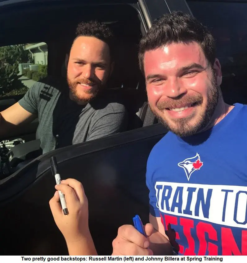 Two men in a car smiling and signing autographs.