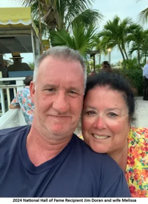 Man and woman smiling outdoors with palms.